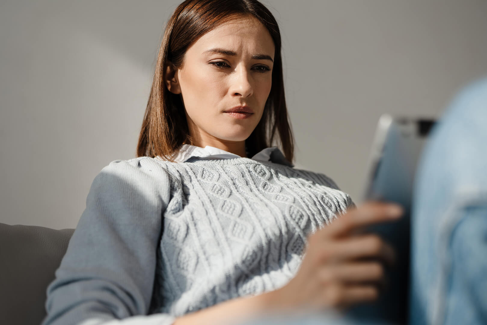 Person sitzt entspannt auf einem Sofa und hält ein Tablet in der Hand.